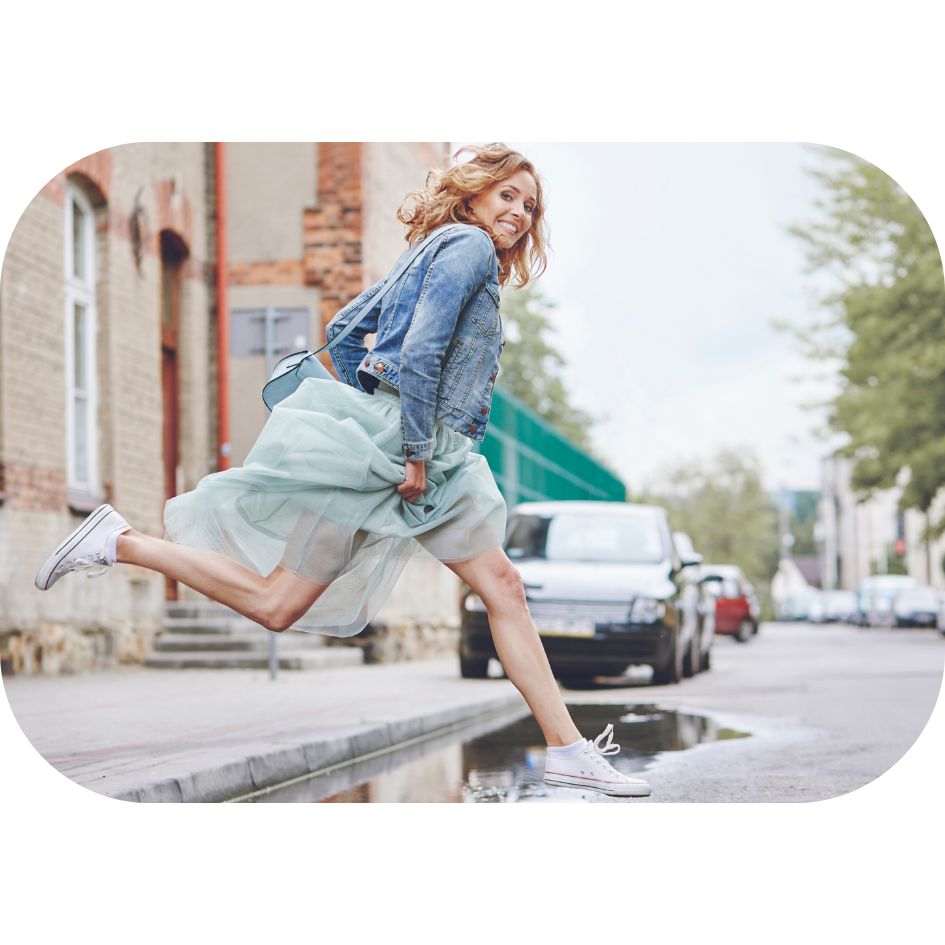 Photo représentant une femme active qui traverse la rue en sautant et avance le sourire.