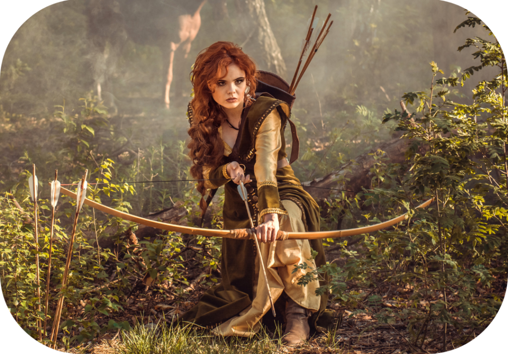 Cette photo montre une femme rousse aux cheveux longs qui s'apprête à tirer à l'arc en bois dans la forêt